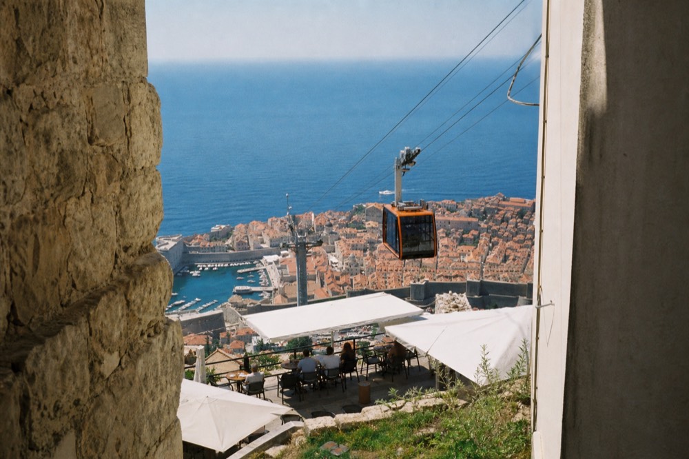 Mountain terrace with tables and umbrellas above a walled city by the sea