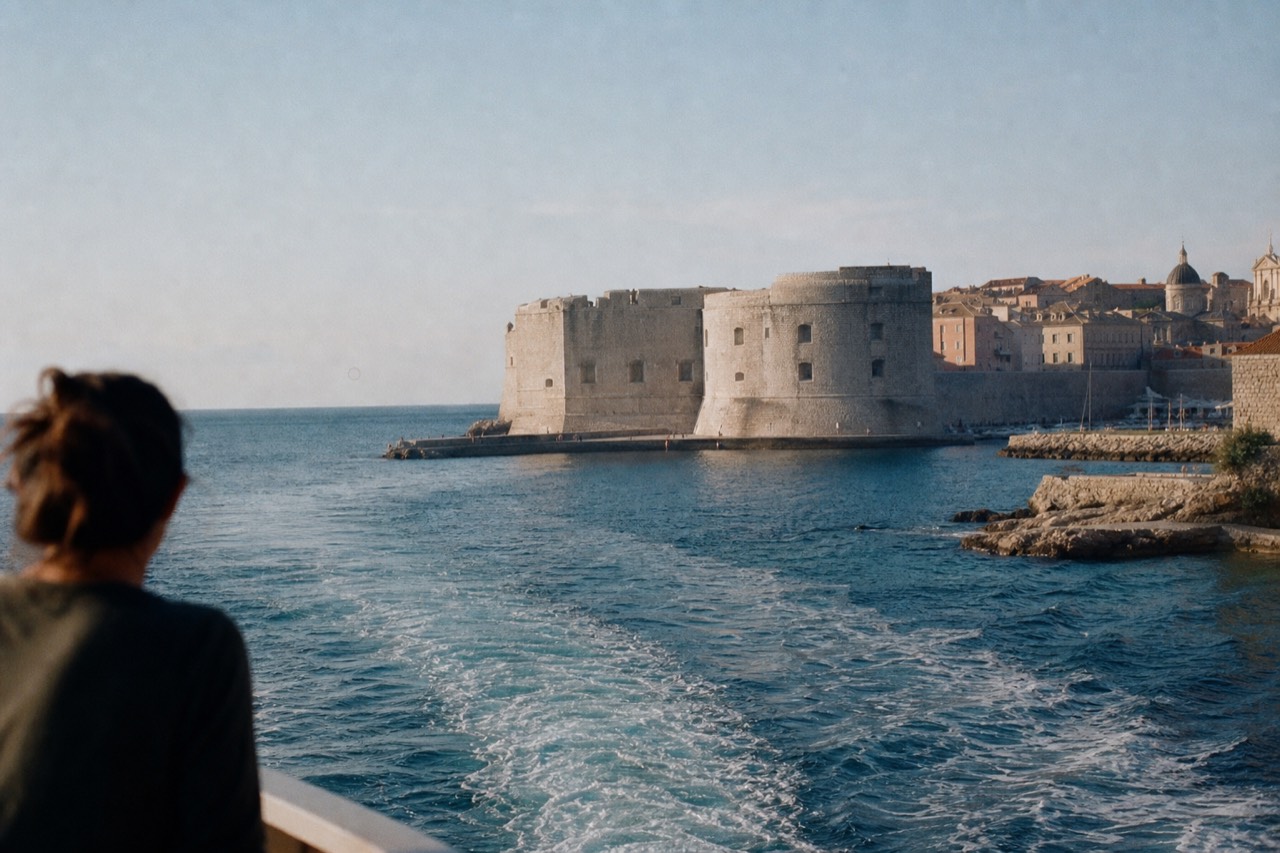 A ferry boat crossing calm blue Adriatic water toward a walled coastal town