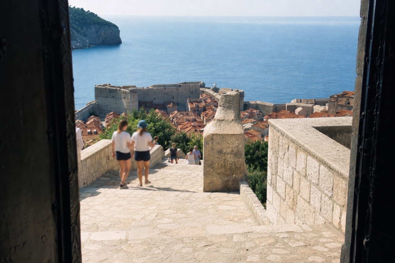 The stone city walls of Dubrovnik above red rooftops with the Adriatic sea beyond