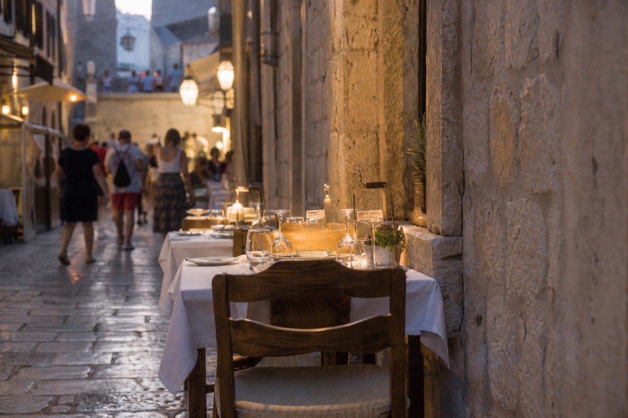 Evening tables set along a stone lane in Dubrovnik with warm light on old walls