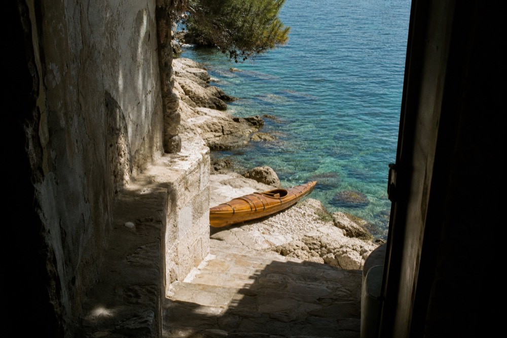 A wooden kayak resting on smooth limestone rocks above translucent turquoise water