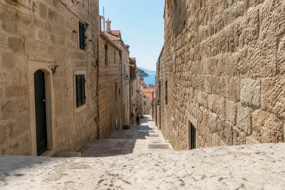 Sunlit limestone street inside Dubrovnik Old Town with shuttered stone buildings