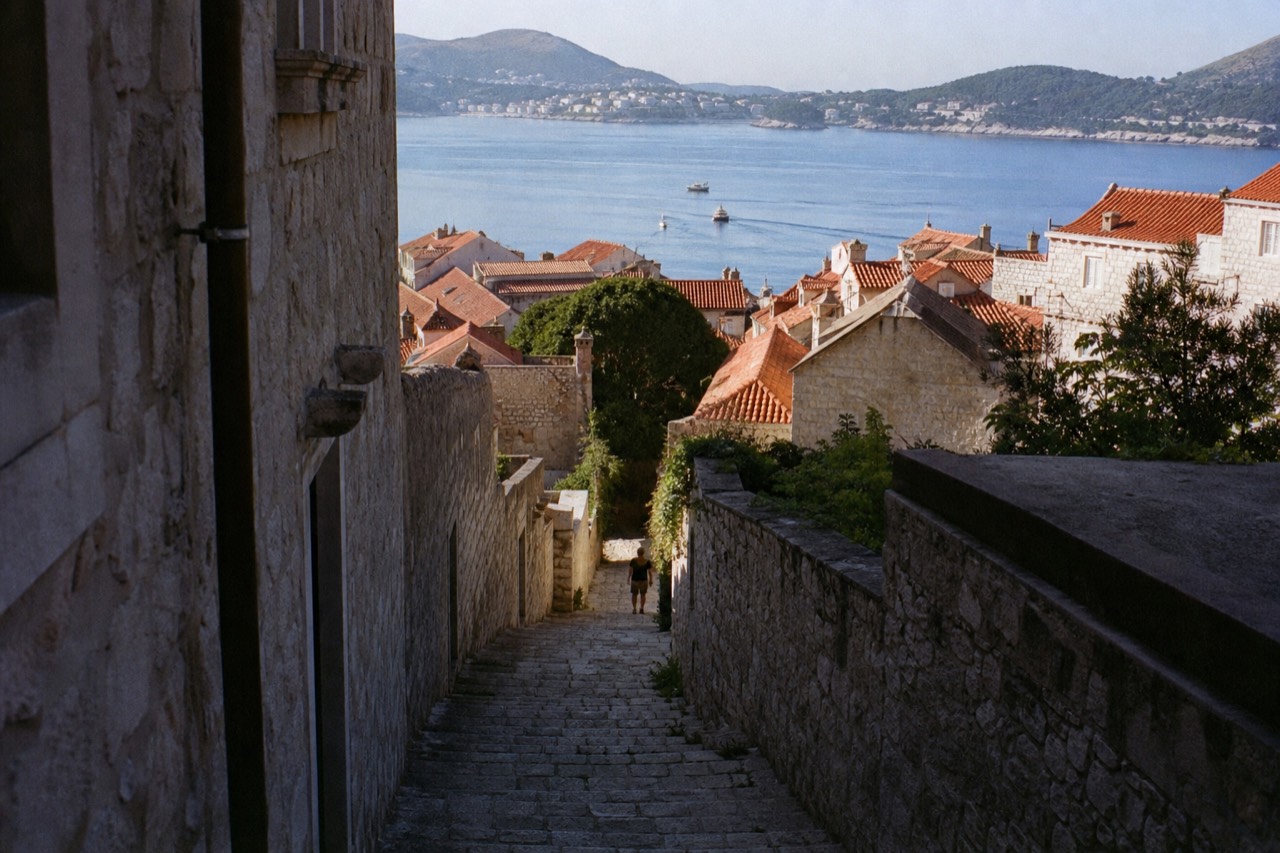Walled old town rooftops above a calm blue Adriatic bay with hills in the distance