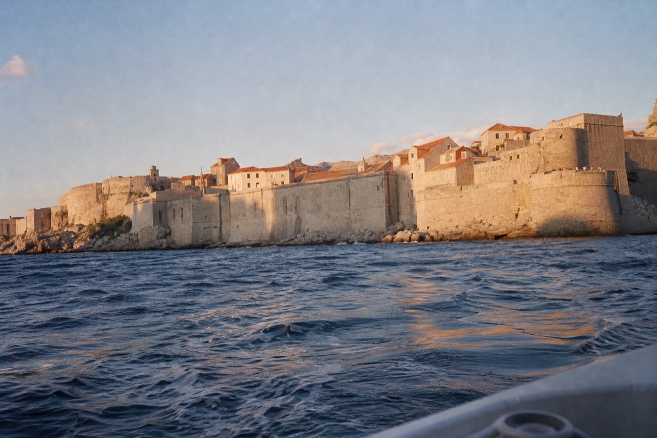 Stone city walls of Dubrovnik rising above red rooftops and the Adriatic sea