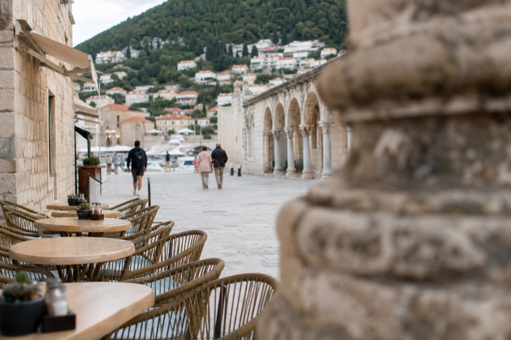Café tables and chairs set out along the wide limestone paving of the Stradun in Dubrovnik