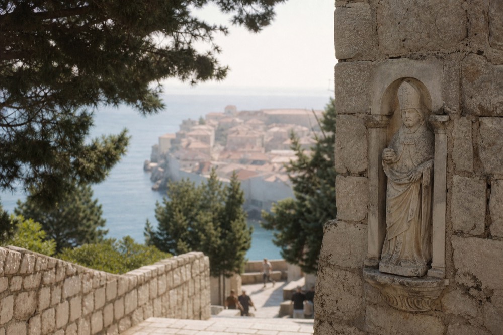 Carved stone figure of a bishop saint set into an old city wall above a stone street