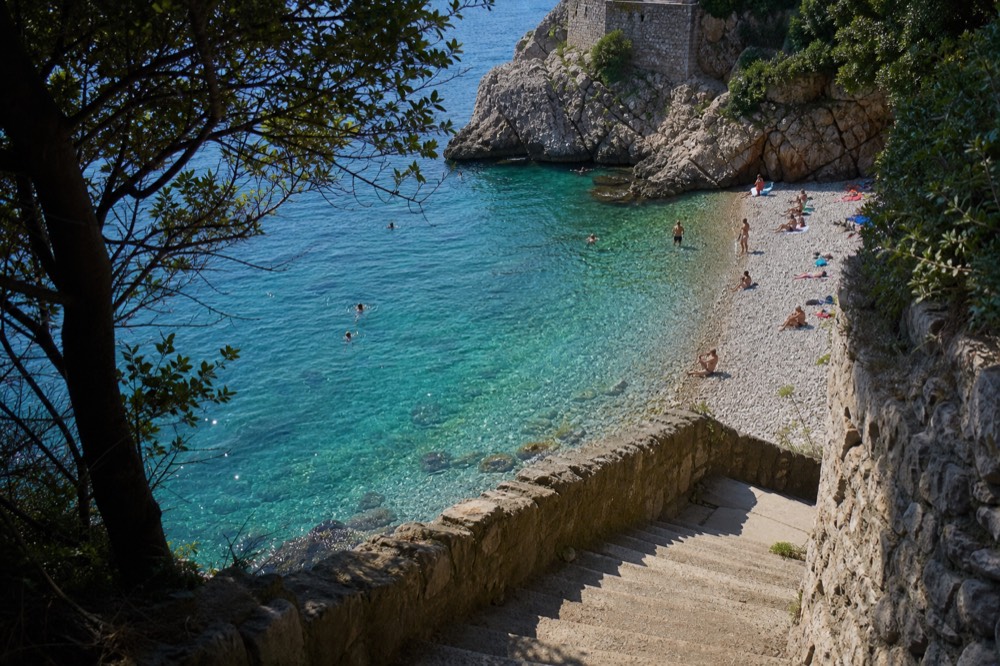 Swimmers in clear turquoise water a few metres from a pebble shoreline