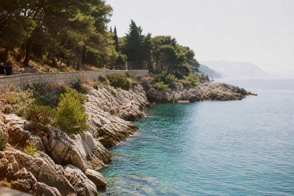 Rocky shoreline with deep blue transparent water and pine trees reaching to the waterline