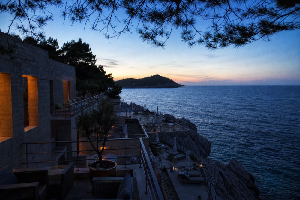 Hotel terraces above a pebble bay with sun loungers facing the evening sea