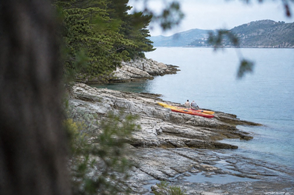 Kayaks resting on a rocky shore with calm evening sea and distant coastline
