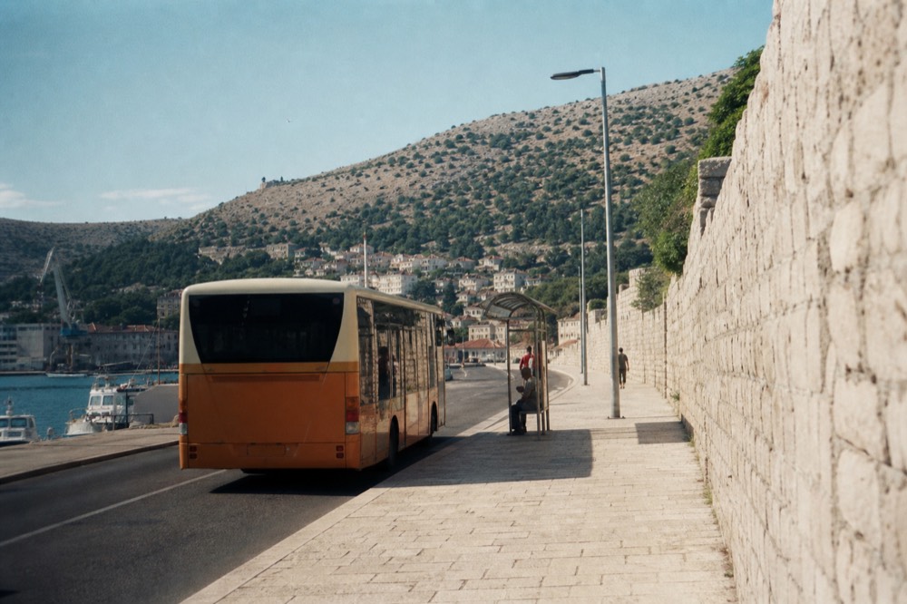 A local bus stopped at a roadside stop with the harbour behind it