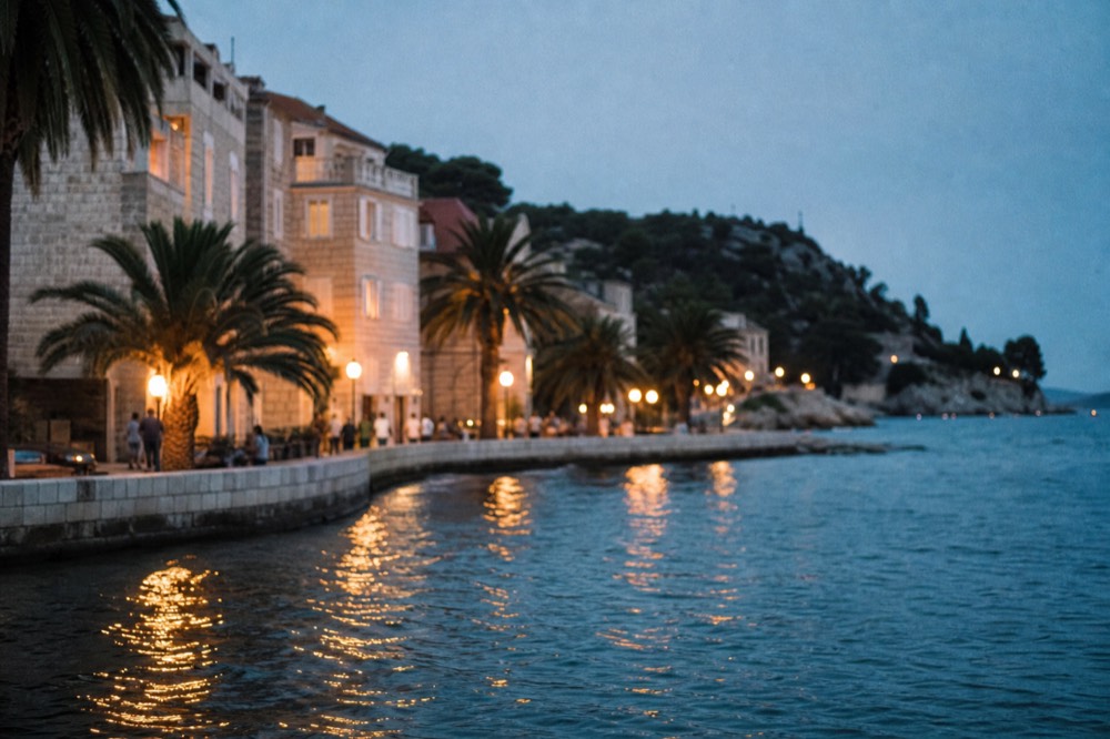 A pedestrian avenue lined with palm trees and stone apartment buildings leading toward the sea