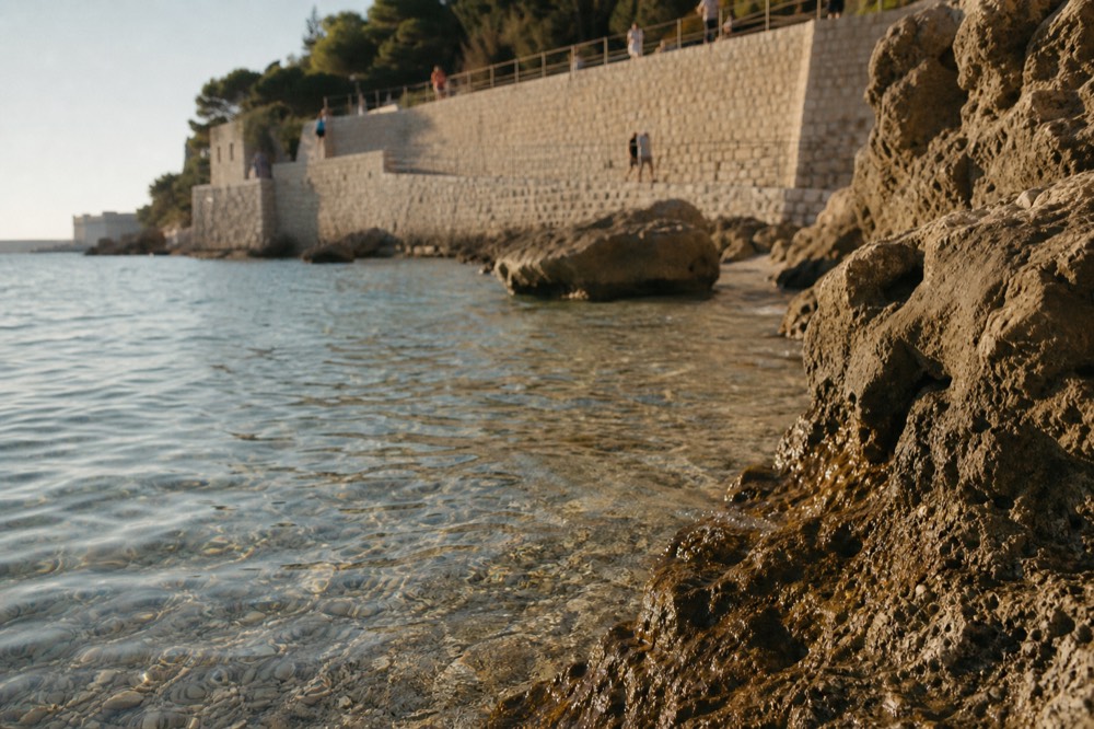 Clear turquoise water over pebbles seen from a low rock at the waterline