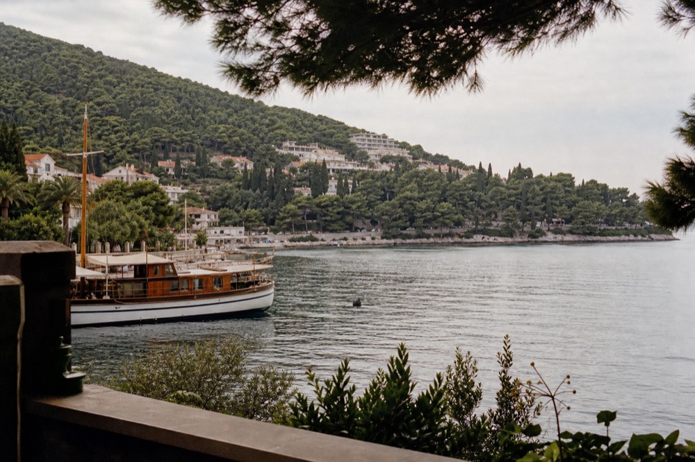 A wooden boat moored in a small harbour with pine-covered hills behind
