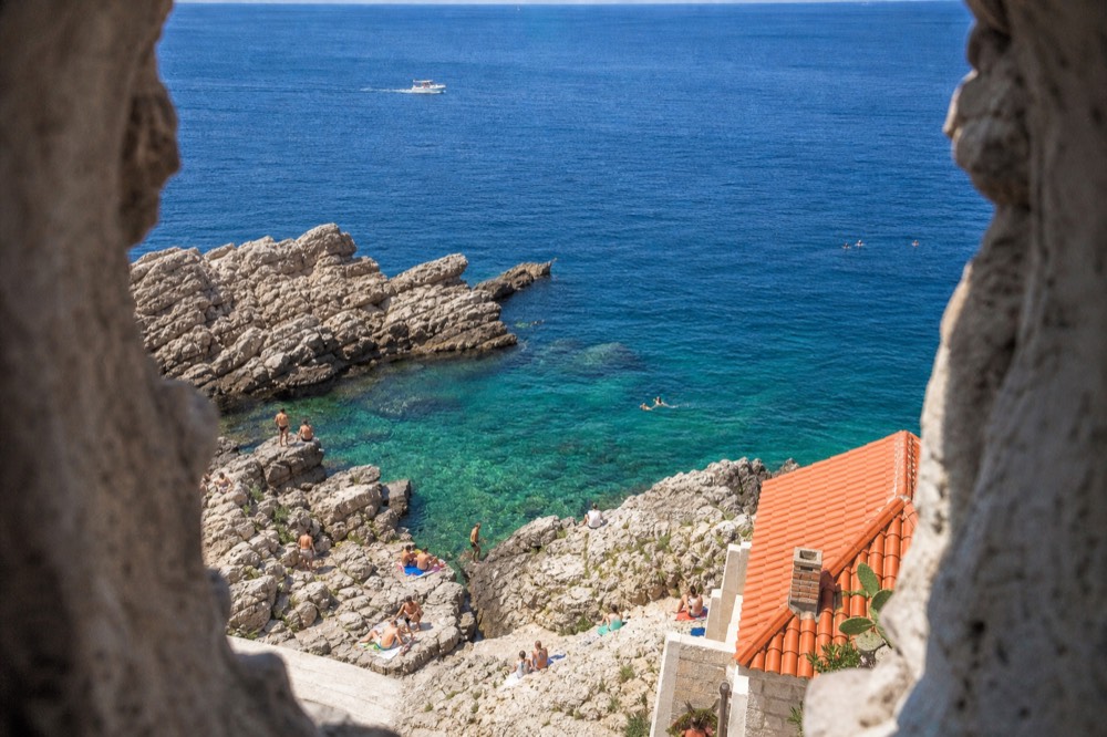 Swimmers in clear turquoise water at a rocky beach near Dubrovnik
