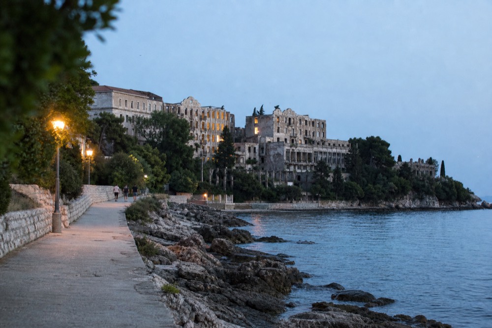Coastal path leading toward ruined hotel blocks above a rocky shoreline