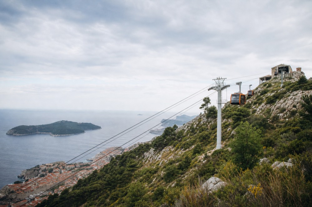 Cable car cabins travelling up the steep slope toward the hilltop station above Dubrovnik