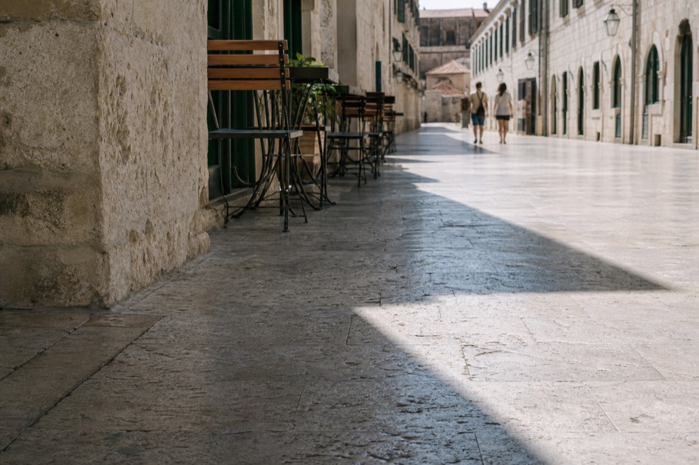 Wide flat stone street in Dubrovnik at morning with cafe tables and closed shutters