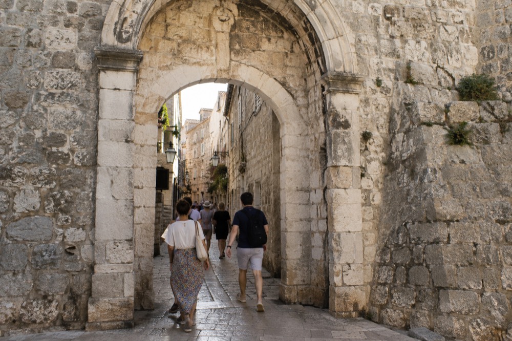 A stone gate archway in a city wall with people walking through it toward narrow streets