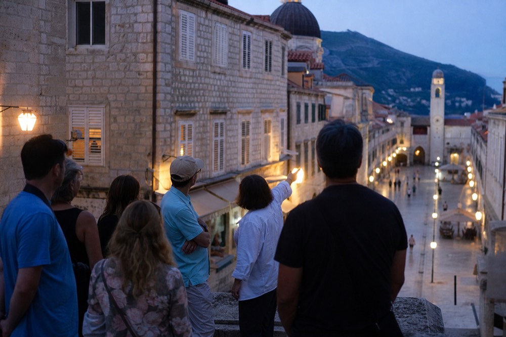 A guide pointing to the city walls while a small group listens on the Stradun