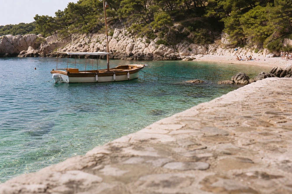 A wooden boat anchored in a bay beside a sandy beach and pine trees