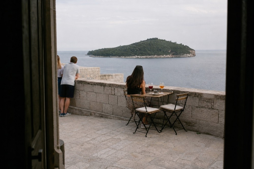 Drinks on a stone terrace at the edge of the city walls with open sea and a distant island beyond