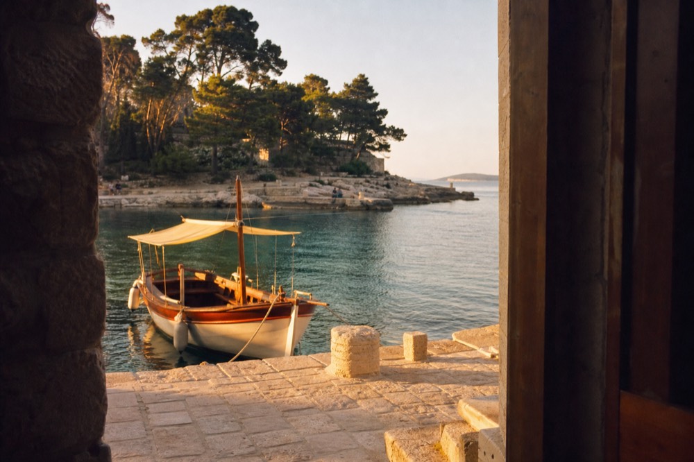 Wooden boat moored at a small island harbour with pine trees and clear water