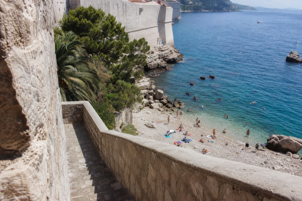 Sunlit Adriatic sea and Dubrovnik city walls seen from above with bathers at a small rocky beach