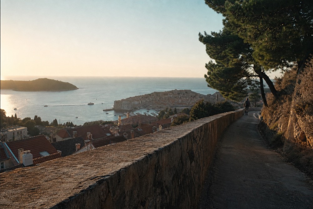 A winding hill road climbing above a red roofed coastal town