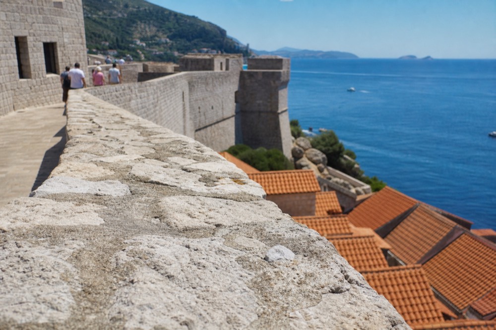 A stone fortress wall above a blue sea with terracotta roofs below