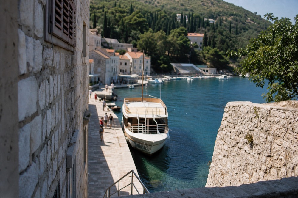 A boat moored in a small harbour beside stone buildings and green hills