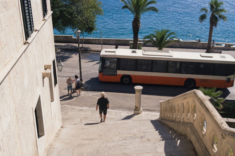 A bus stopped on a coastal street with palm trees and sea beyond