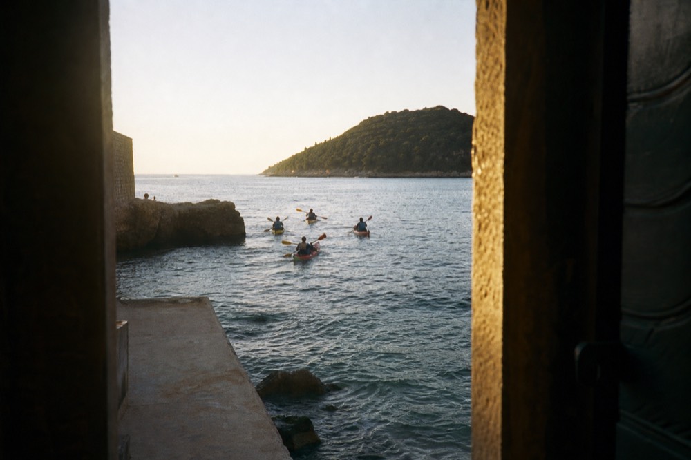 Sea kayaks paddling along a stone coastline toward a green island