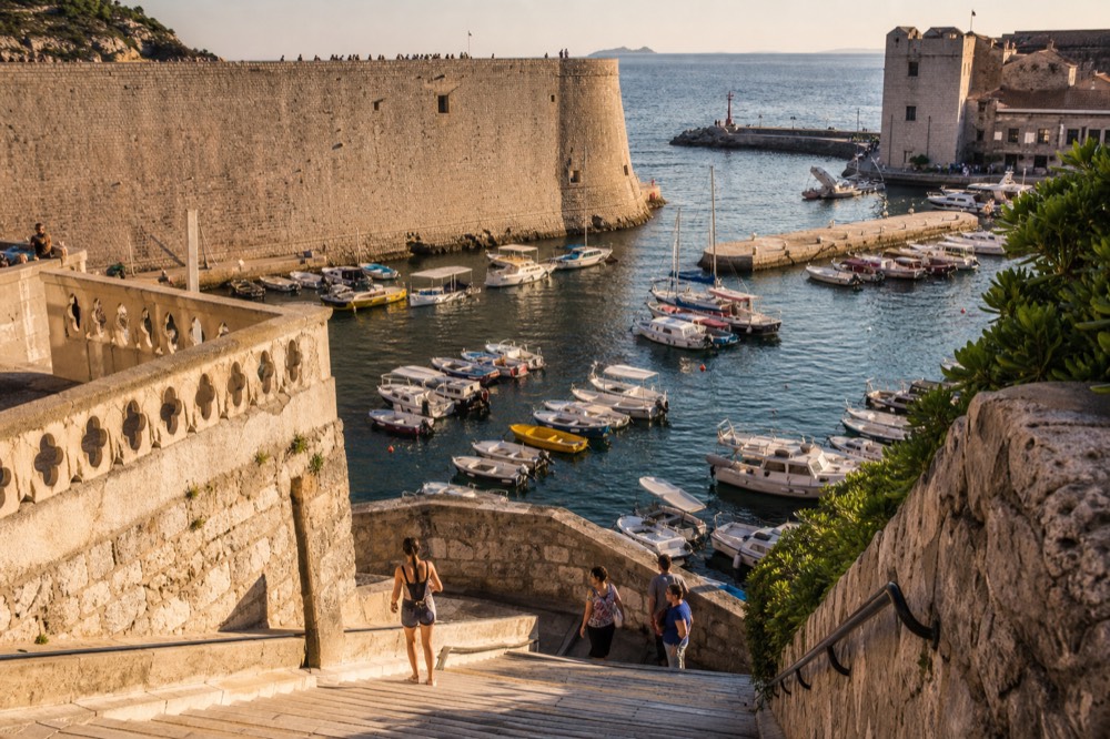 A small harbour filled with boats beneath tall stone walls at dusk