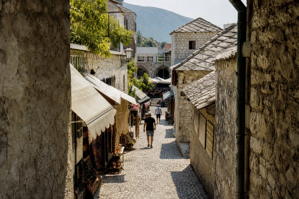 A narrow stone street in bright summer sun with awnings and shopfronts