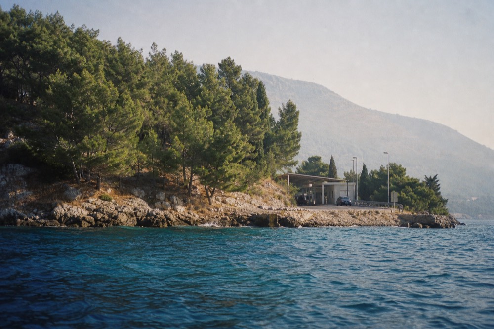 A road winding along a coastline with a small border checkpoint ahead