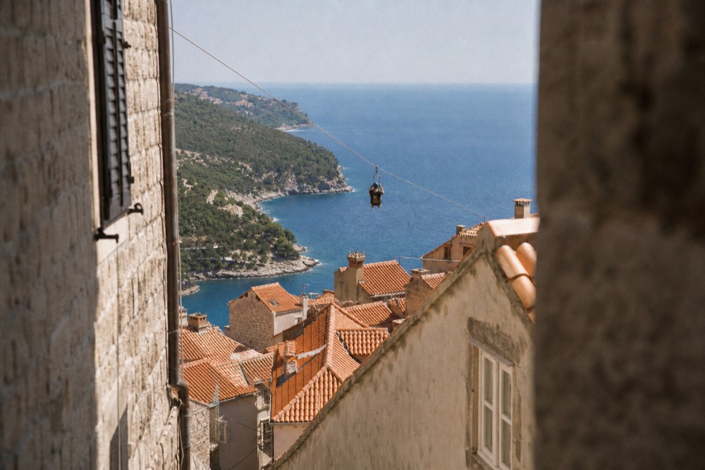 A person in a harness riding a zipline above a hillside with the sea in the distance