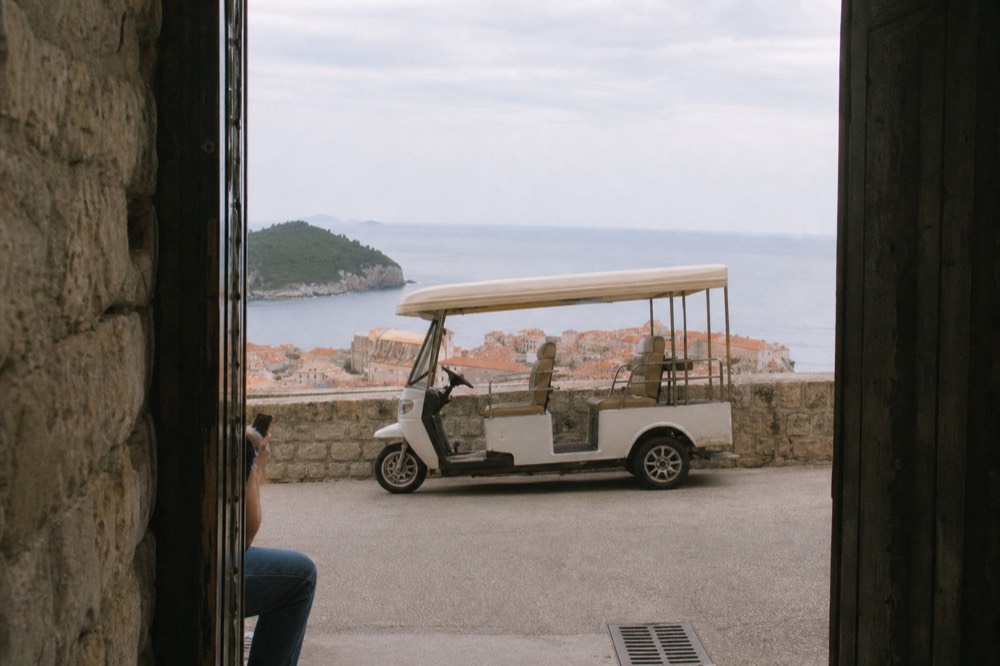 An open-sided electric tuk tuk vehicle parked on a road with a view over Dubrovnik rooftops