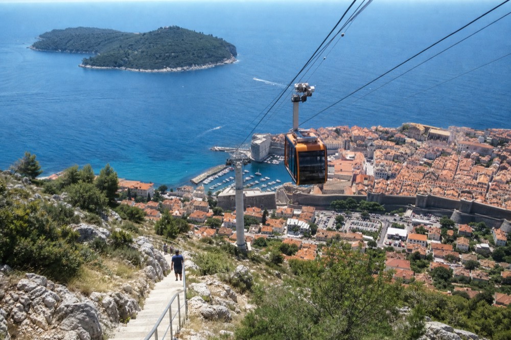 A cable car cabin ascending a steep cable above a hillside toward a mountaintop station