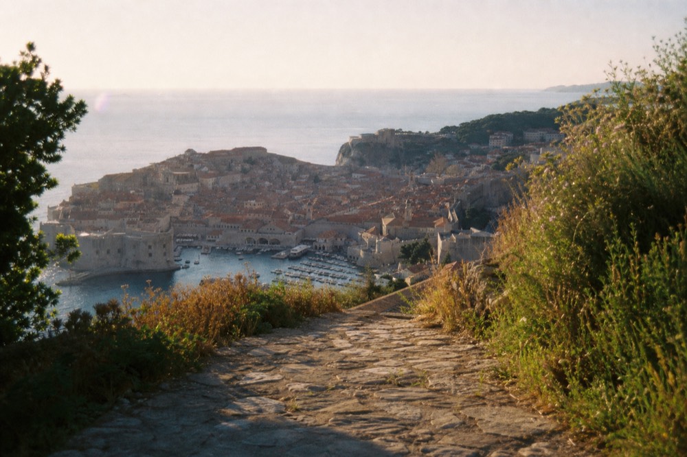 A wide view of Dubrovnik Old Town walls and red rooftops seen from a hillside at golden hour