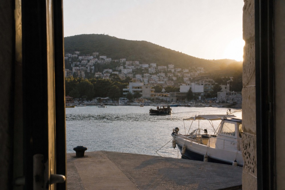 Evening light over a harbour with moored boats and a hillside town behind
