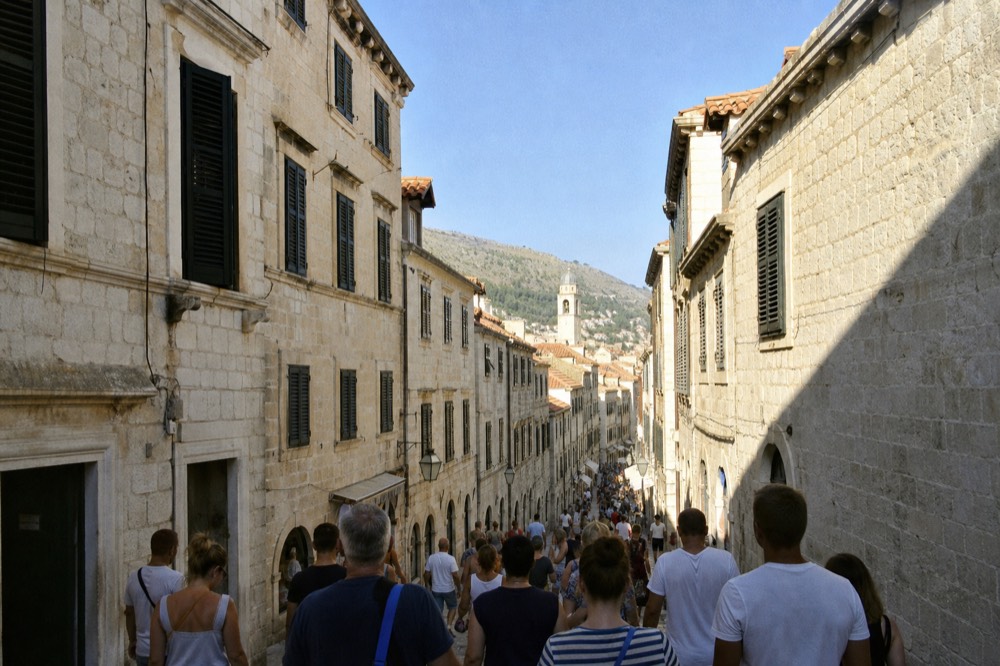 A crowded limestone street in Dubrovnik Old Town filled with visitors walking in summer sunshine