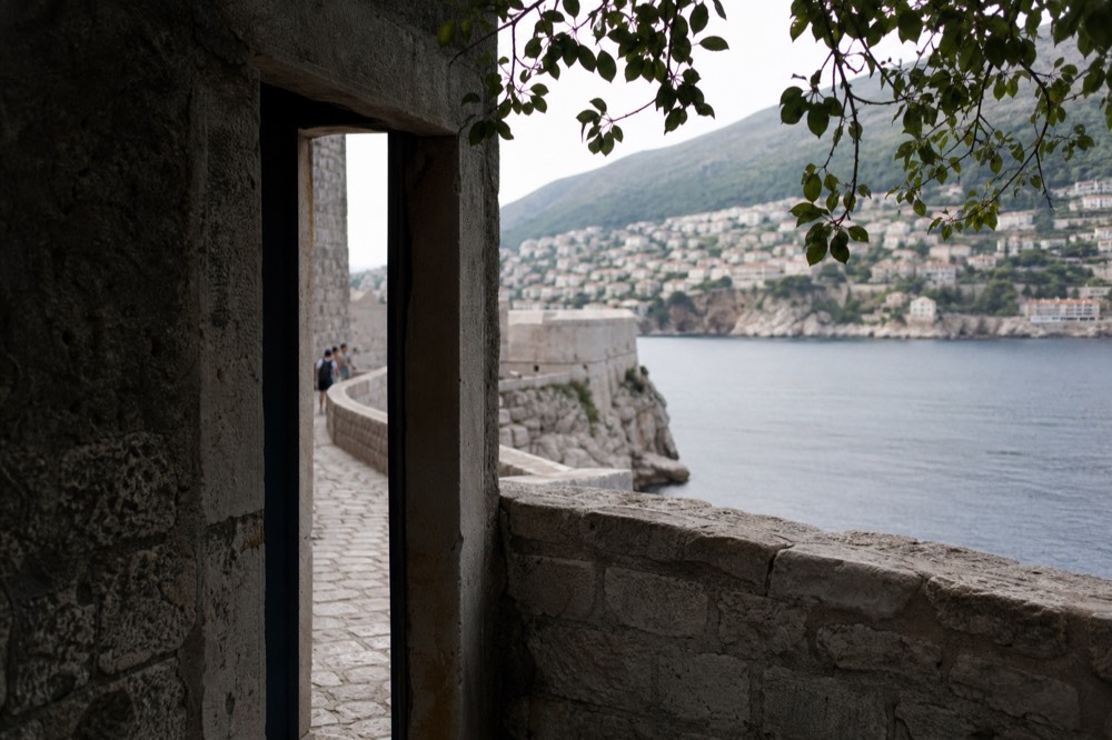 A narrow stone doorway in a high city wall opening toward a sunlit cliff terrace