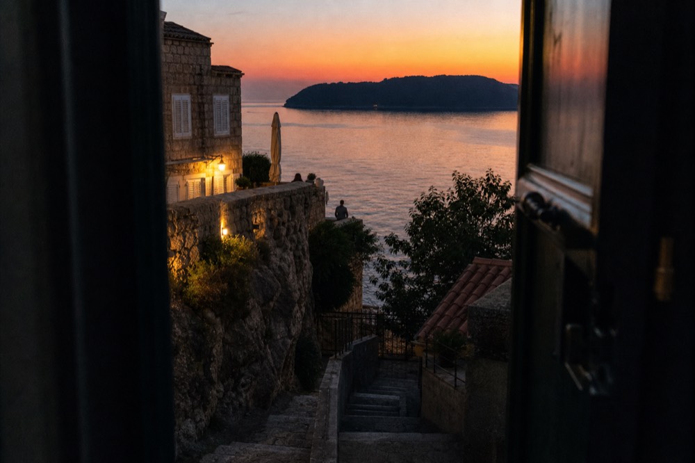 A cliff terrace at sunset with the sea glowing orange below a dark island silhouette
