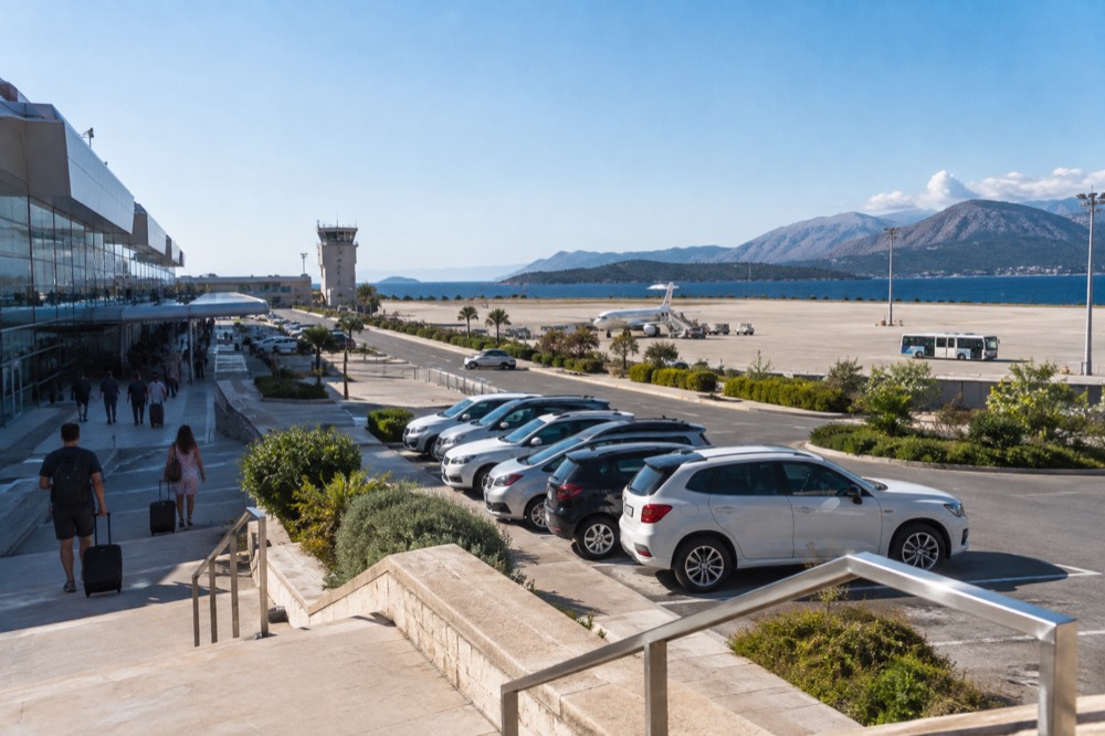 A row of rental cars parked outside Dubrovnik Airport terminal with the sun shining on the concrete apron