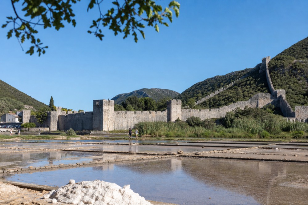 The medieval stone walls of Ston with the salt pans in the foreground and a clear blue sky above