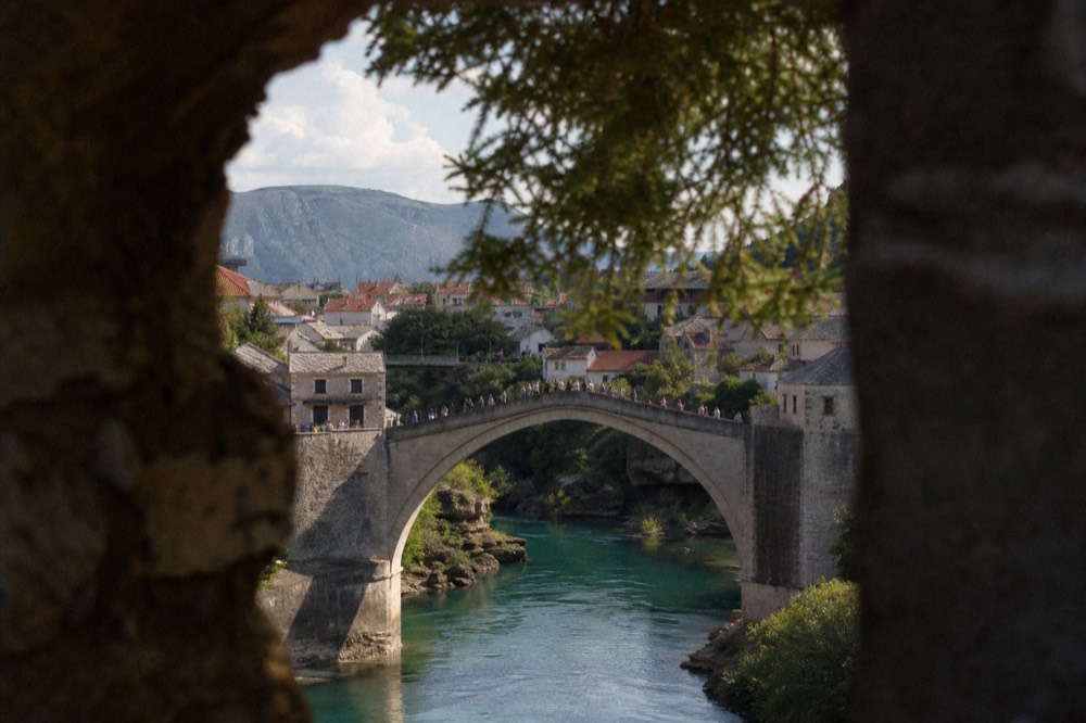 The Old Bridge in Mostar with the turquoise Neretva River below and a small crowd of pedestrians crossing
