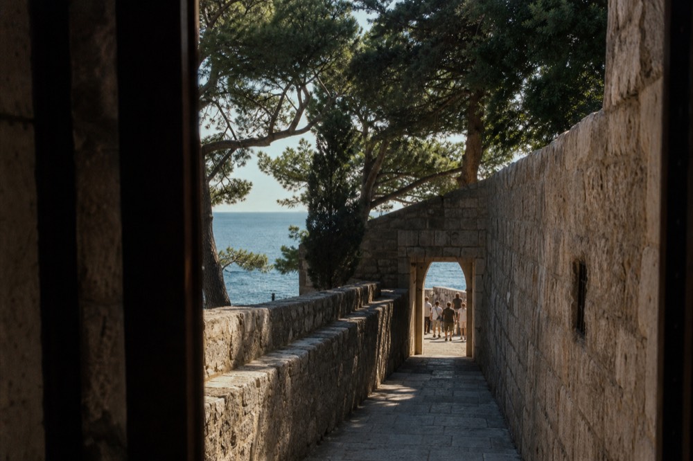 A narrow stone lane inside Dubrovnik Old Town leading toward a doorway in the city wall