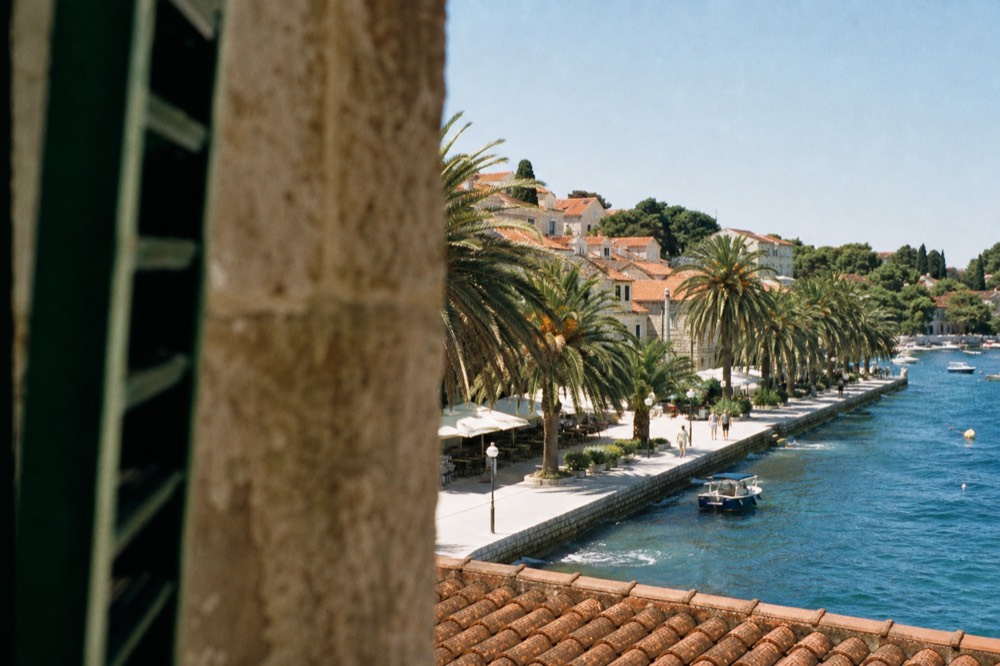 Palm-lined seaside promenade with cafe tables and stone buildings