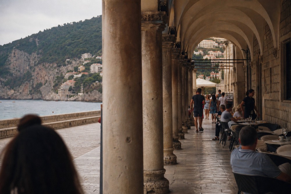 A busy Dubrovnik street in late afternoon with cafés and pedestrians under stone arches